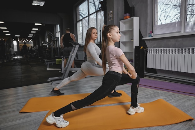 Schönes Teenager-Mädchen, das sich vor dem Training mit ihrem persönlichen Trainer im Fitnessstudio aufwärmt