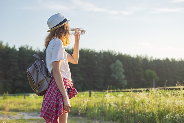 Schönes Teenager-Mädchen im Hut mit Rucksackflasche des frischen Wassers