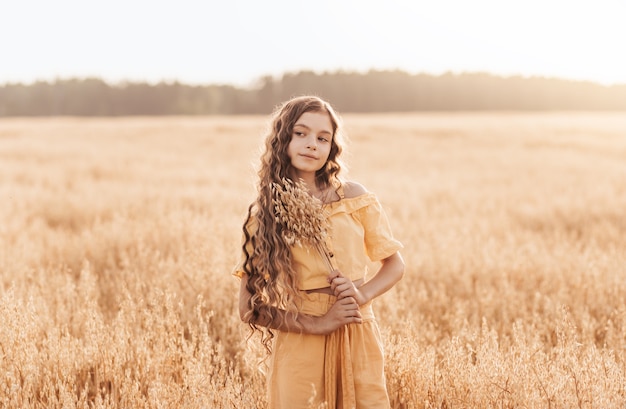 Schönes Teenager-Mädchen mit langen Haaren, das an einem sonnigen Tag durch ein Weizenfeld geht. Porträt im Freien. Schulmädchen entspannt