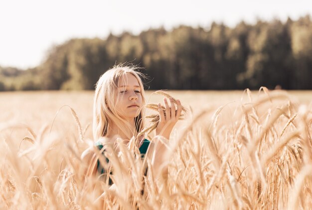 Schönes Teenager-Mädchen mit langen weißen Haaren, das an einem sonnigen Tag durch ein Weizenfeld geht?