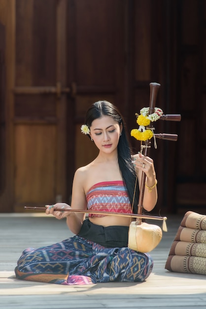Schönes thailändisches Mädchen im thailändischen traditionellen Kostüm mit thailändischer Geige