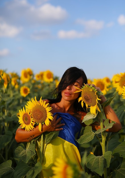 Foto schönes ukrainisches mädchen, das in einem sonnenblumenfeld steht und in eine nationalflagge gehüllt ist