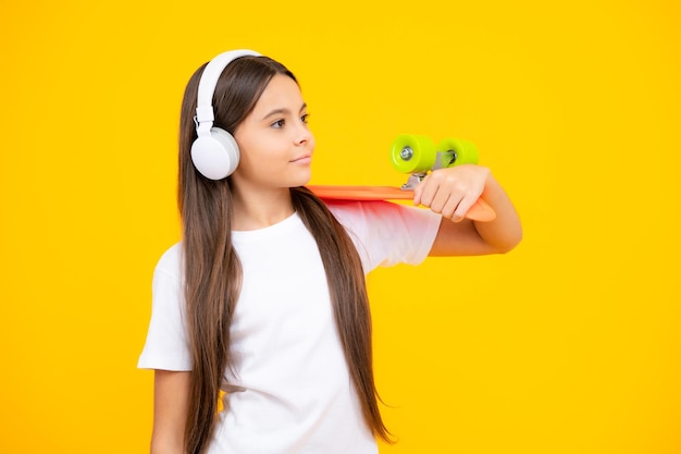 Schönes und modisches junges Teenager-Mädchen, das mit Skateboard und Kopfhörern posiert Teenager Street Fashion Lifestyle