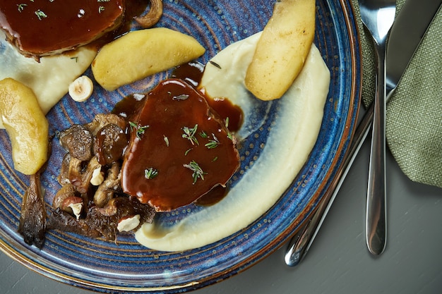 Schönes und saftiges Steak aus Kalbsfilet (Rinderfilet) mit Sauce garniertes Selleriecremepüree auf einem blauen Teller auf einem Holztisch. Draufsicht. Flach liegen