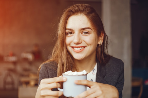 schönes und stilvolles Mädchen, das in einem Café sitzt und einen Kaffee trinkt