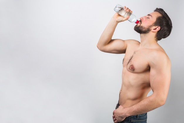 Schönes und wundervolles Bild eines gutaussehenden Mannes, der sehr nahe an einer weißen Wand steht und etwas Wasser aus der Flasche trinkt. Er genießt den Moment.