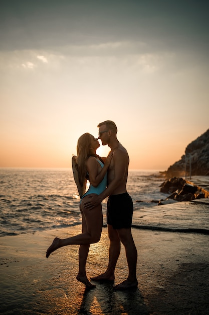 Schönes verliebtes Paar auf dem Hintergrund des Sonnenuntergangs am Meer. Junge Frau und Mann umarmen sich bei Sonnenuntergang am Meer