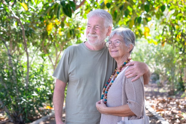 Schönes weißhaariges Seniorenpaar, das im Wald umarmt und in die Natur schaut Lächelnde ältere Großeltern genießen einen gesunden Lebensstil im öffentlichen Park