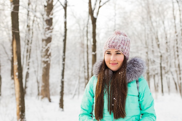 Schönes Winterporträt der jungen Frau in der verschneiten Winterlandschaft