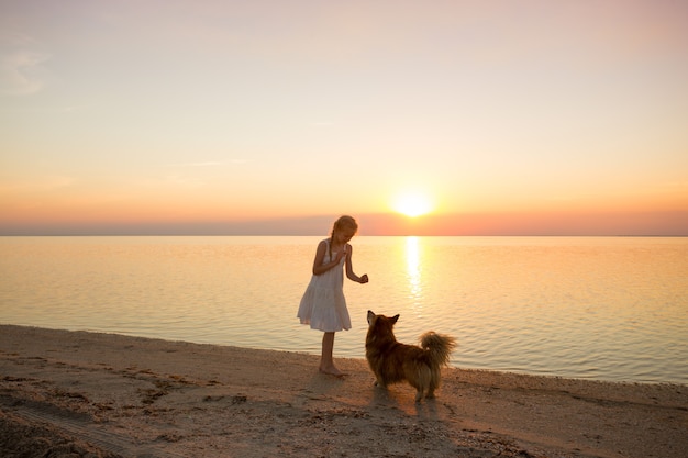 Schönes Wochenende am Meer - kleines Mädchen geht bei Sonnenuntergang mit einem Hundecorgi am Meer spazieren. Ukrainische Landschaft am Asowschen Meer, Ukraine