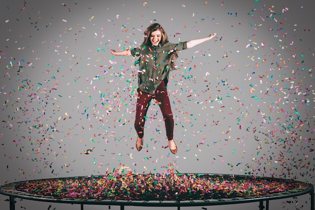 Schönheit auf dem Trampolin. Luftaufnahme einer schönen jungen Frau, die mit Konfetti um sie herum auf Trampolin springt