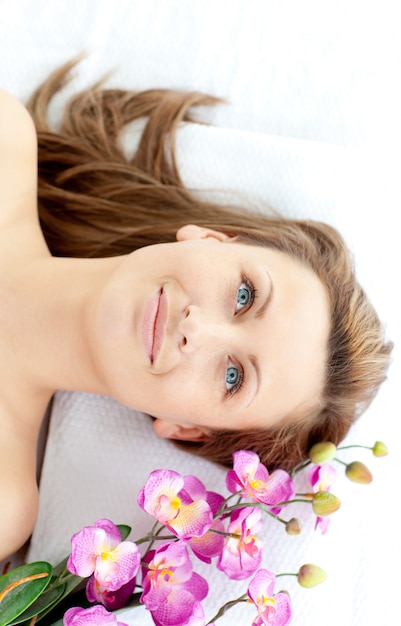 Schönheit, die auf einer Massagetabelle mit Blumen liegt