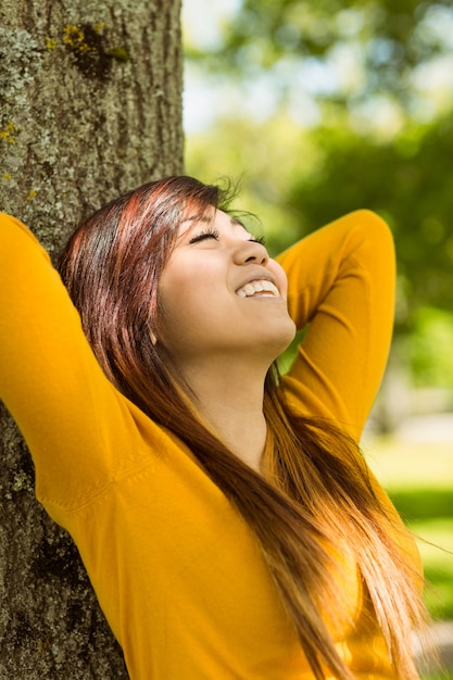 Schönheit, die gegen Baum im Park sitzt