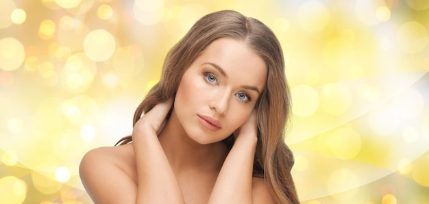 Schönheit, Menschen, Haarpflege, Urlaub und Gesundheitskonzept - schönes Gesicht der jungen Frau über gelbem Lichthintergrund