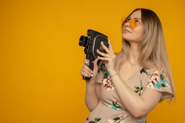 Schönheit mit Filmkamera. Fröhliche junge Frau mit Filmkamera und posiert vor gelbem Hintergrund