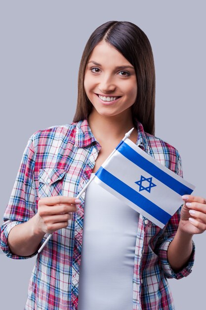 Schönheit mit israelischer Flagge. Glückliche junge Frauen, die die Flagge Israels halten, während sie vor grauem Hintergrund stehen