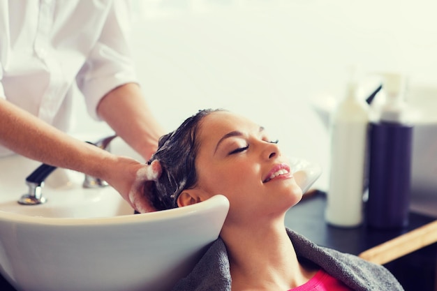 Schönheit und Menschenkonzept - glückliche junge Frau mit Friseurin, die den Kopf im Friseursalon wäscht
