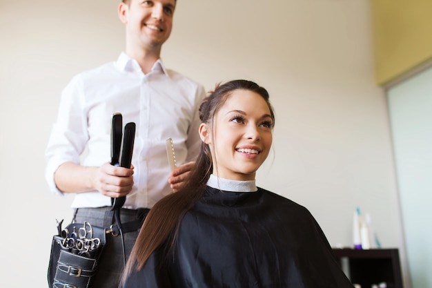 Schönheits-, Frisur- und Personenkonzept - glückliche junge Frau mit Friseur, der Haare kräuselt und Frisur im Salon macht