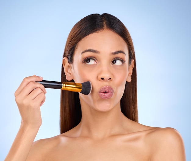 Schönheits-Make-up und Pinsel mit einer Frau im Studio für kosmetische Zufriedenheit und Selbstpflege. Leuchtende Grundierung und Rouge mit einem Mädchenmodell auf blauem Hintergrund für Gesichtspuder und Kosmetikprodukte