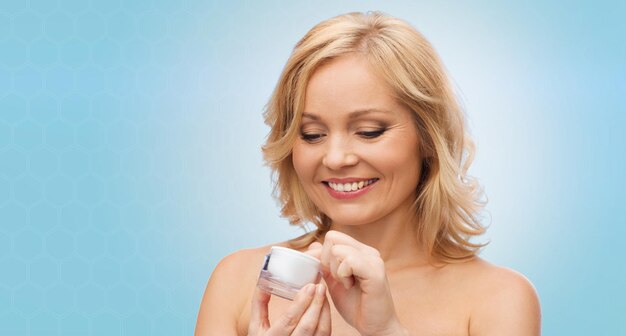Schönheits-, Menschen-, Hautpflege- und Kosmetikkonzept - glückliche Frau mit Cremetiegel auf blauem Hintergrund