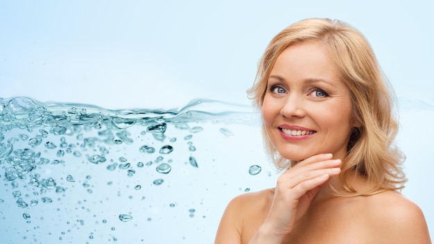 Schönheits-, Menschen- und Hautpflegekonzept - lächelnde Frau mittleren Alters mit nackten Schultern, die das Gesicht über Wasserspritzer mit Luftblasenhintergrund berühren
