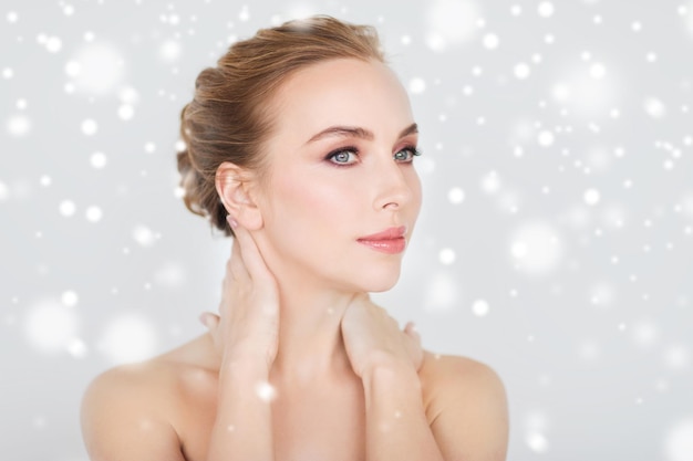 Schönheits-, Menschen-, Winter- und Körperpflegekonzept - schönes Gesicht und Hände einer jungen Frau vor grauem Hintergrund und Schnee