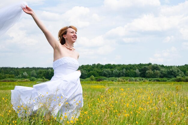 Schönheits-Naturkonzept des Hochzeitstages In der Mitte des Feldes gibt es eine erstaunliche Frau, die ein weißes Brautkleid trägt, das sie um sich selbst dreht und Pailletten leuchten im Licht der Sonne