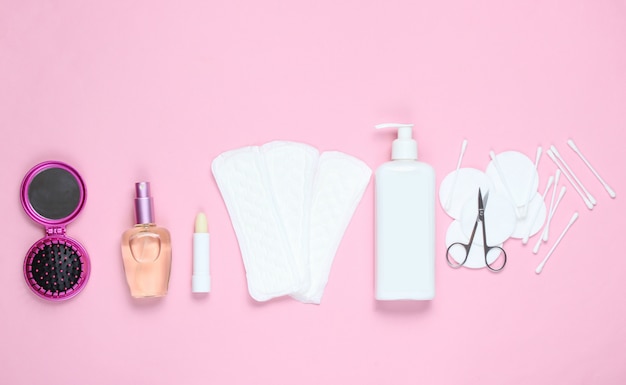 Schönheits- und Hygieneprodukte der Frauen auf rosa Pastellhintergrund. Parfümflasche, hygienischer Lippenstift, Pads, Flaschencreme, Nagelschere.