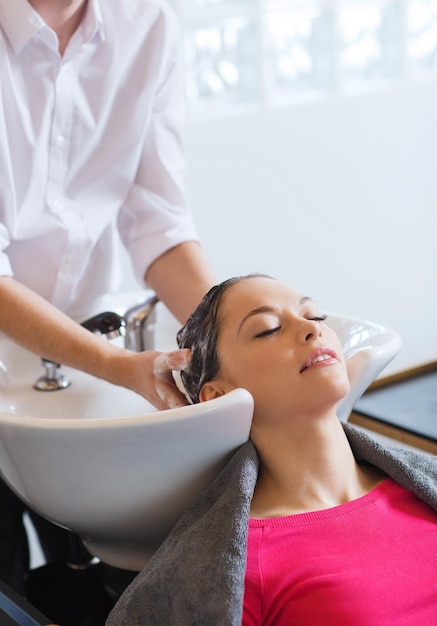Schönheits- und Leutekonzept - glückliche junge Frau mit waschendem Kopf des Friseurs am Friseursalon