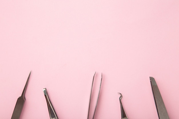 Schönheits- und Modekonzept - Werkzeuge für das Wimpernverlängerungsverfahren. Pinzette auf rosa Hintergrund. Copyspace-Modell. Ansicht von oben