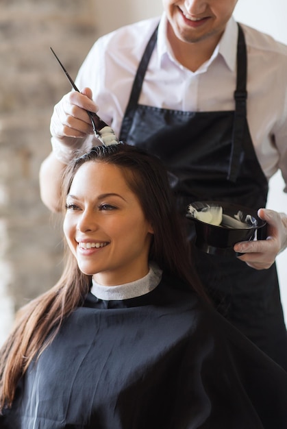 schönheits- und personenkonzept - glückliche junge frau mit friseur, der haare im salon färbt