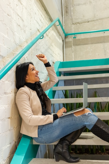 Schönheitsbrünette Frau arbeitet mit ihrem Laptop von der Treppe