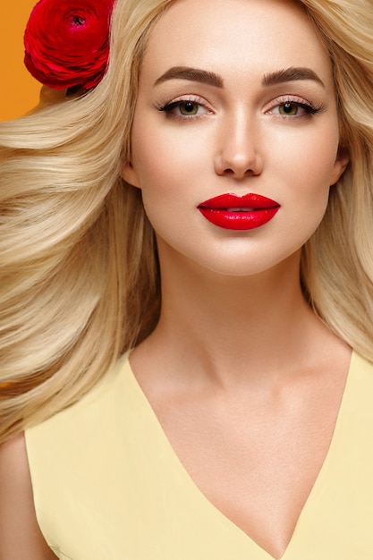 Schönheitsfrau mit langen lockigen blonden Haaren Blumenhaar manikürte Nägel trendige Farben orange und gelb