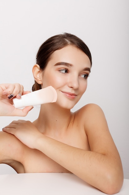 Schönheitsgesicht der jungen Frau mit kosmetischer Creme auf einer Wange.