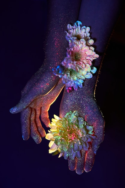 Schönheitshände einer Frau im ultravioletten Licht mit Blumen in den Handflächen. Kosmetik für die Handhautpflege