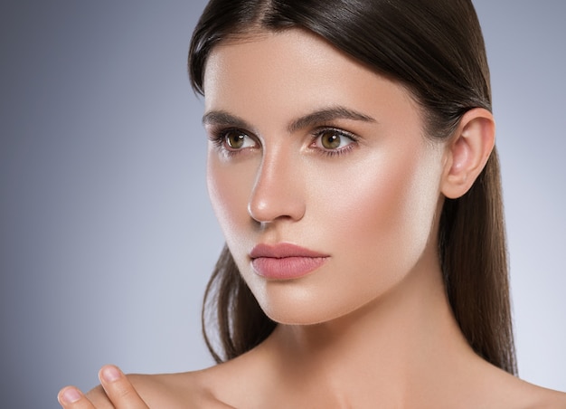 Schönheitshautfrauengesicht gesunde Haut schönes Modell Nahaufnahme Gesicht natürliches Make-up Brunettehaar. Farbiger Hintergrund. Studioaufnahme.