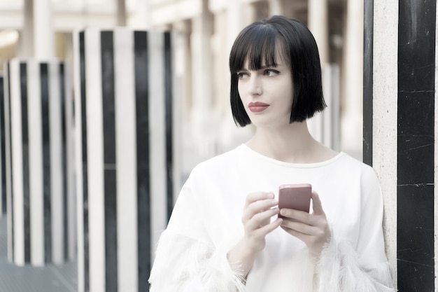 Schönheitsmädchen mit sexy Blick in Paris, Frankreich. Frau mit roten Lippen verwenden auf dem Smartphone. Frau mit brünetten Haaren halten Handy. Modemodell mit mobilem Gerät. Neue Technologie für das moderne Leben.