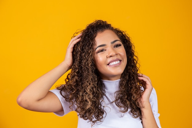 Schönheitsporträt der afroamerikanischen Frau mit Afro-Frisur und Glamour-Make-up. Brasilianische Frau. Gemischtrassig. Lockige haare. Frisur. Gelber Hintergrund