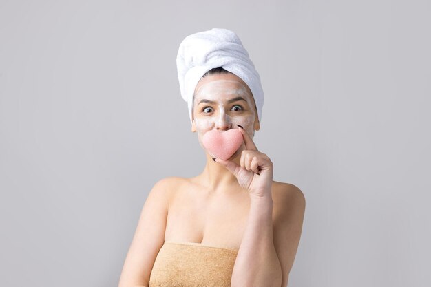 Schönheitsporträt der Frau im weißen Handtuch auf dem Kopf trägt Creme auf das Gesicht auf Hautpflegereinigung