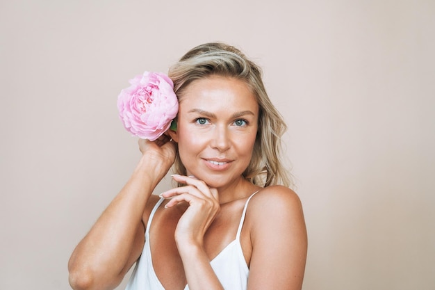 Schönheitsporträt der lächelnden jungen Frau des blonden Haares mit der rosa Pfingstrose in der Hand lokalisiert auf weißem Hintergrund