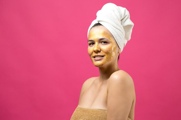 Schönheitsporträt einer Frau in weißem Handtuch auf dem Kopf mit goldener Pflegemaske im Gesicht Hautpflege-Reinigung Öko-Bio-Kosmetik-Spa-Relax-Konzept