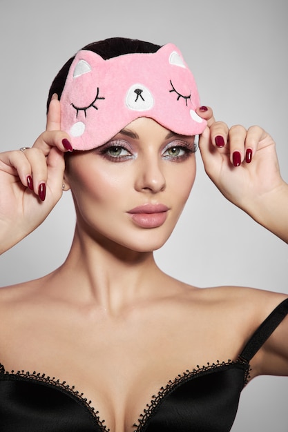 Schönheitsporträt einer Frau mit einer Schlafmaske und rosa zartem Make-up auf ihren Lippen und Augen. Sexy Brünette Mädchen in Unterwäsche