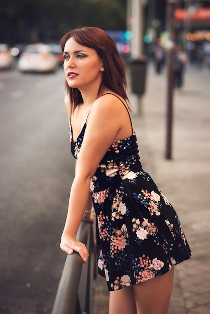 Schönheitsrothaarigemädchen in der Straße, die ein Blumenkleid trägt