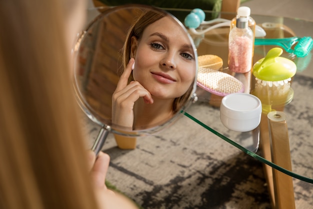 Foto schönheitstag. frau mit handtuch, die ihre tägliche hautpflege zu hause macht. tragen sie feuchtigkeit und creme auf und betrachten sie ihr spiegelbild. konzept der schönheit, selbstpflege, kosmetik, jugend.