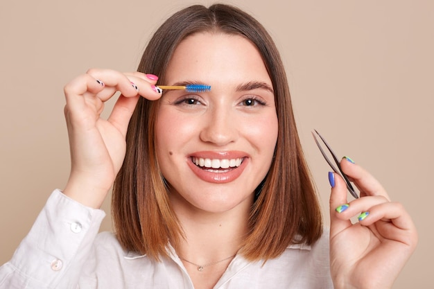 Schönheitswerkzeuge Nahaufnahme einer lächelnden Frau mit professionellem perfektem Make-up, die eine Pinzette hält, die Brauenhaare zupft Metallpinzette für Augenbrauen, die positive Emotionen ausdrücken