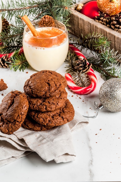 Schoko-Crinkle-Plätzchen zu Weihnachten mit Eierlikör-Cocktail, Zuckerstange, Weihnachtsbaum und Festtagsdeko auf weissem Marmortisch,