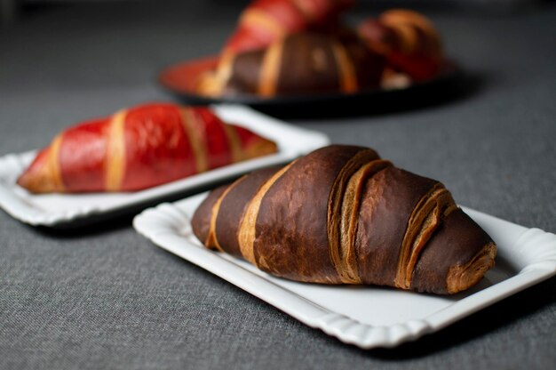 Schokolade und rote Croissants liegen auf Tellern auf einem grauen Tuch Nahaufnahmebrötchen