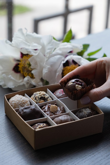 Schokoladen-Bastelbonbons in weiblicher Hand und Pralinenschachtel mit Blumen