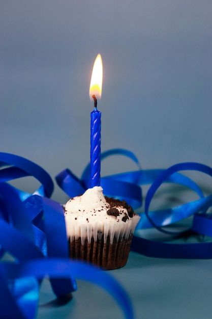 Schokoladen-Cupcake mit blauer Kerze, blauem Hintergrund und blauem Band