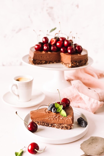 Schokoladen-käsekuchen und ein geschnittenes stück käsekuchen, dekoriert mit frischen kirschen, blaubeeren und einer tasse kaffee. vertikal